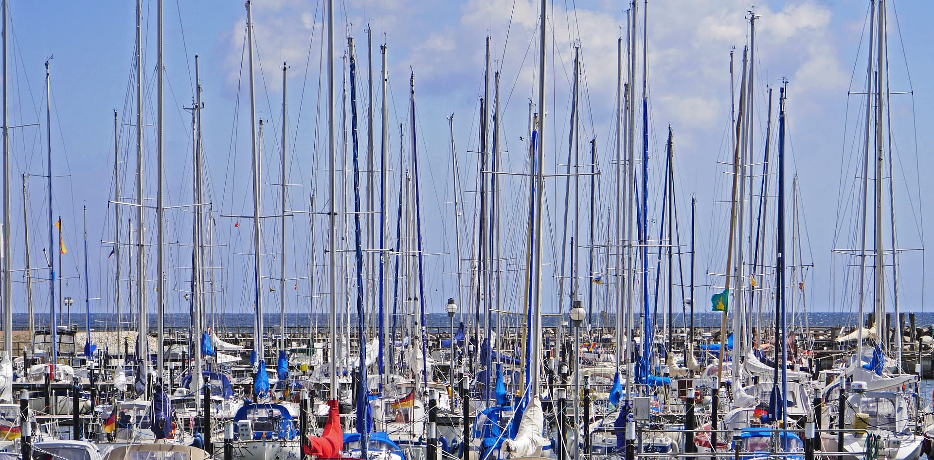 Purjeveneiden mastoja pienvenesatamassa. / Sailboat masts in a seaside port.