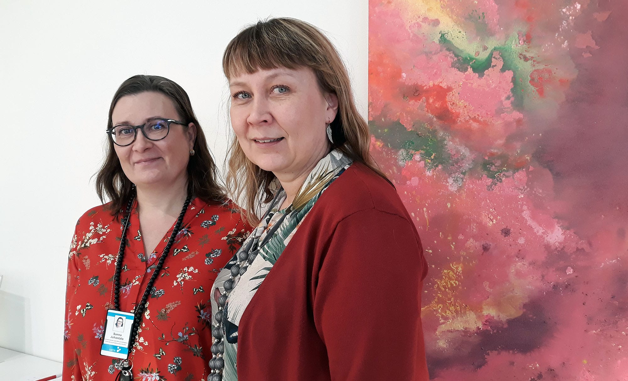 Sanna Juhantalo and Johanna Kares-Koskinen standing front of red painting.