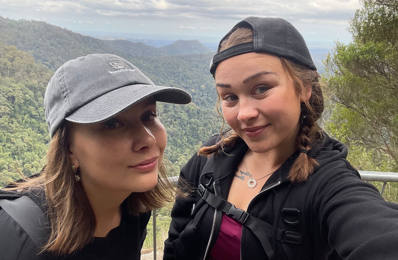 Kaksi naista hymyilee kameralle, taustalla vuoria.