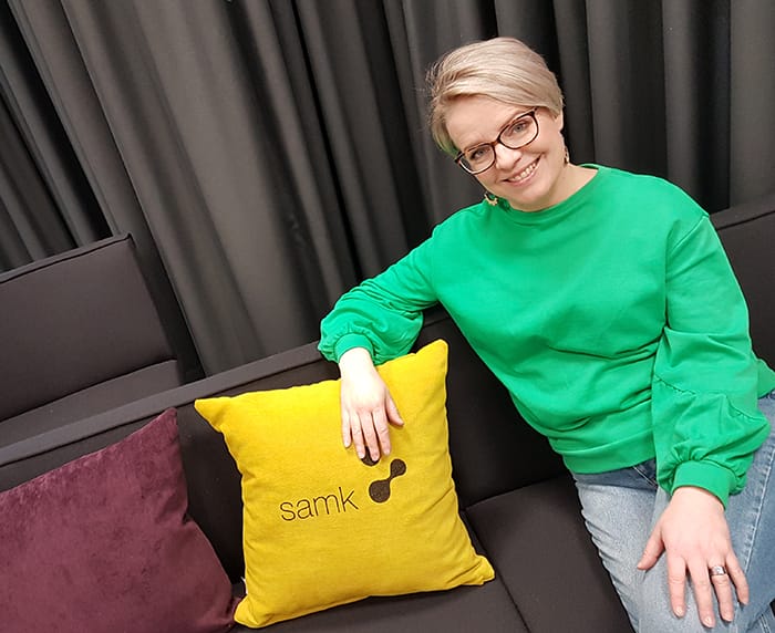 Jonna Koivisto sitting on a couch beside yellow pillow.