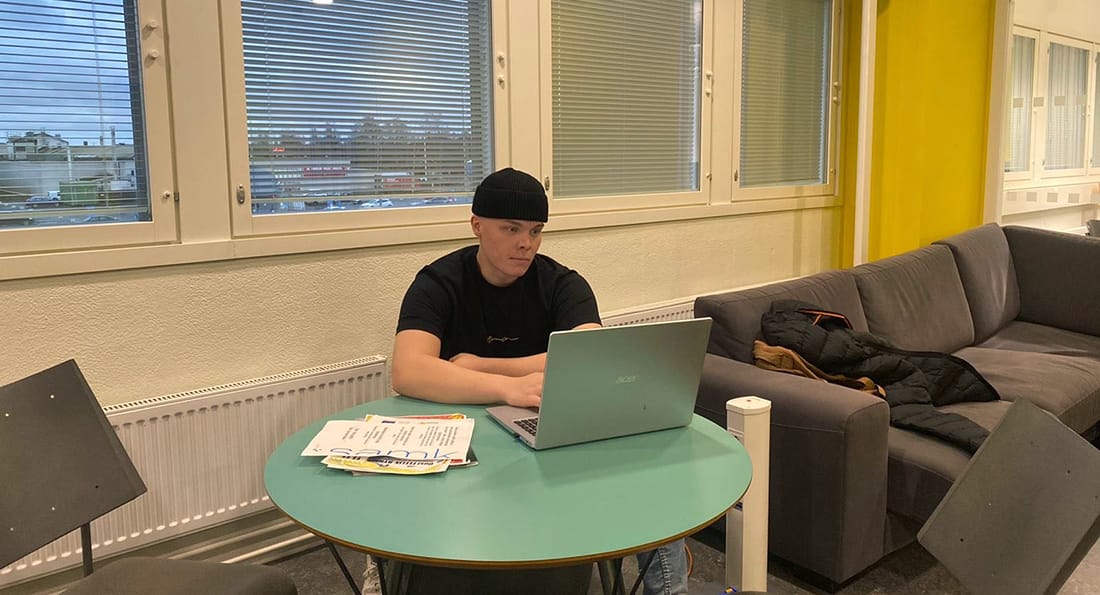 Jere Kuljula istuu pyöreän pöydän vieressä ja katsoo kannettavaa tietokonetta.