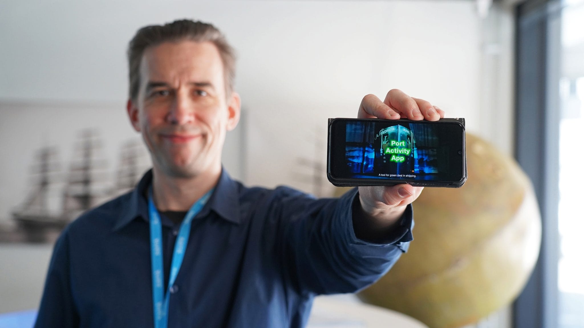 Petteri Hyvärinen holding a mobile phone with the competition video on the screen.