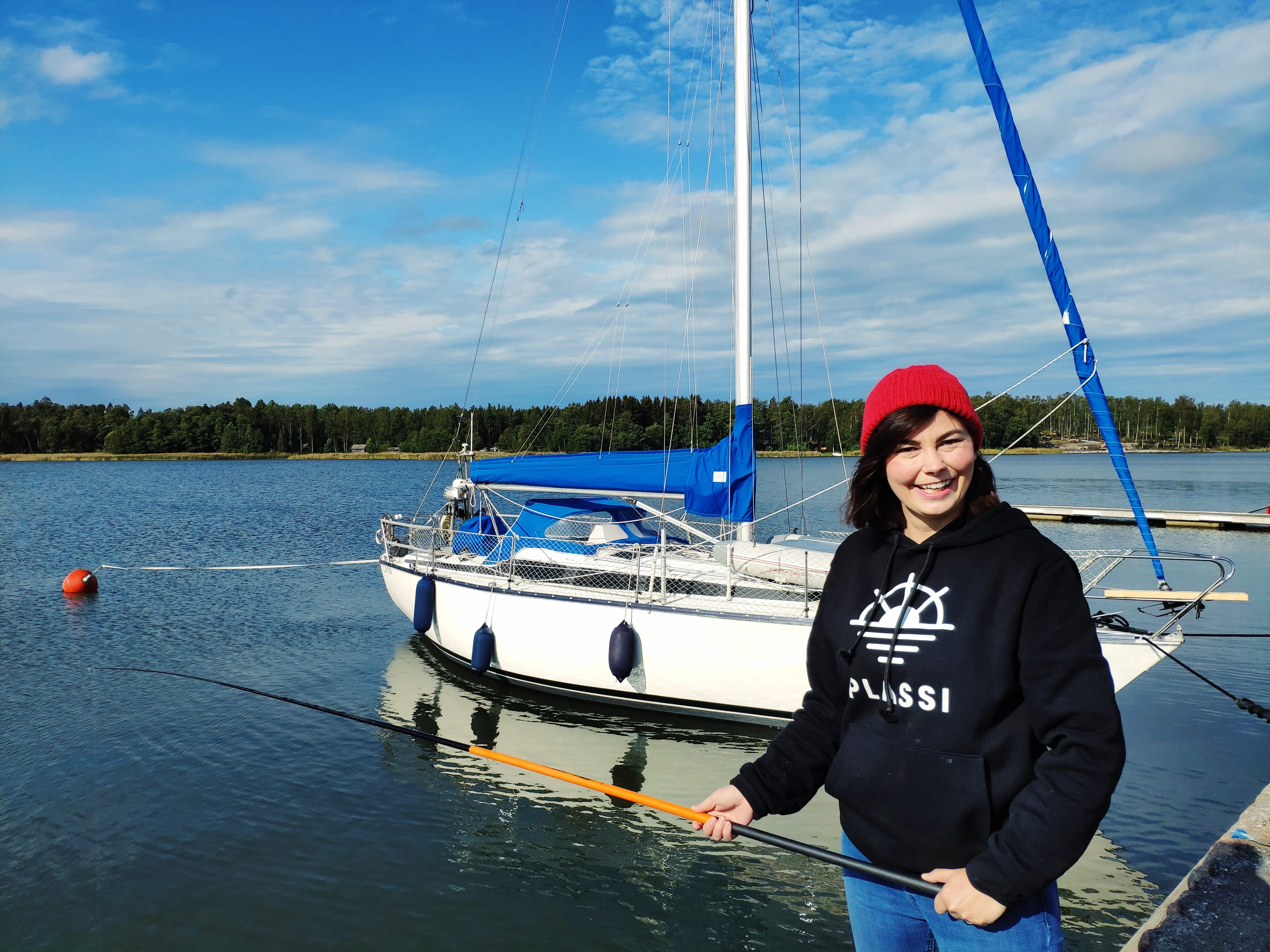 Young woman posing with a fishing rod. In the background is a sailboat.