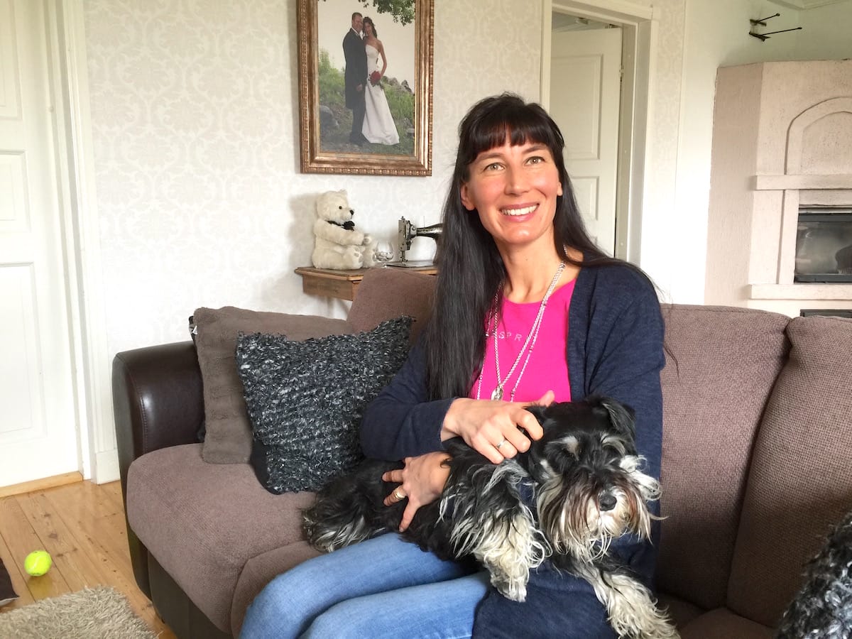 Kuntoutuksen ohjaaja (AMK) Monica Tiisala istuu sohvalla sylissään koira.
