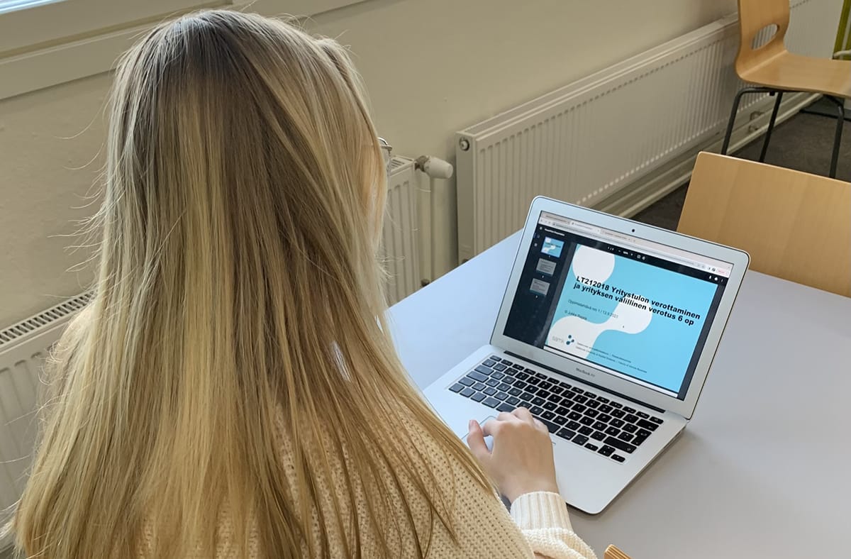 Petra Karttimi selin kameraan kannettavan tietokoneen ääressä.