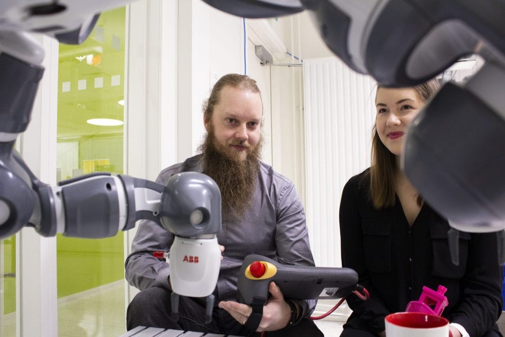 RoboAI-labrassa kaksi opiskelijaa taustalla, etualalla robottikäsi.