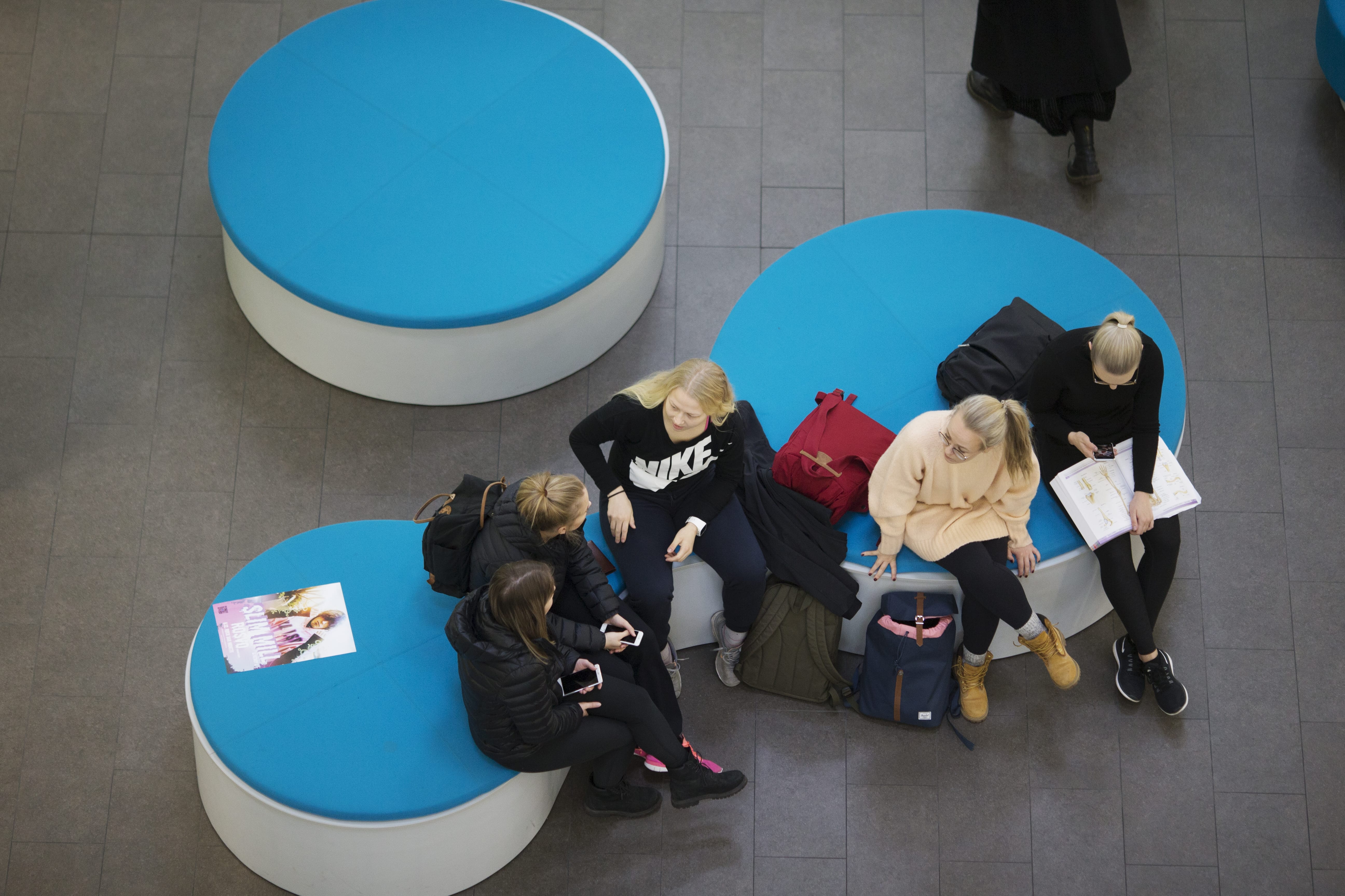 Opiskelijoita istuu logopenkeillä SAMK-kampus Porin aulassa, kuva ylhäältäpäin.