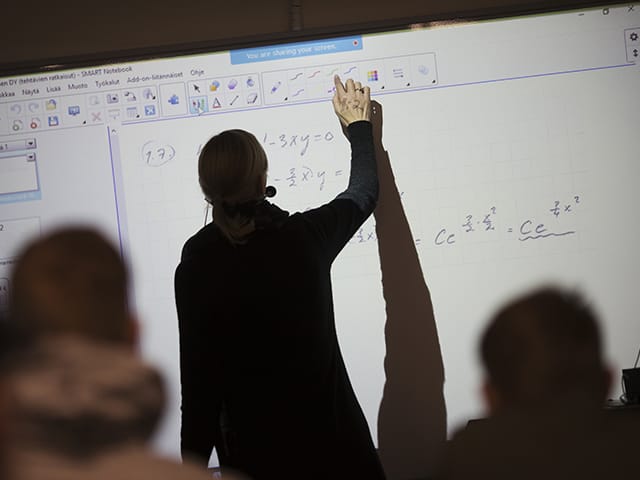 Opettaja näyttää laskutoimituksia älynäytöltä opiskelijoille.