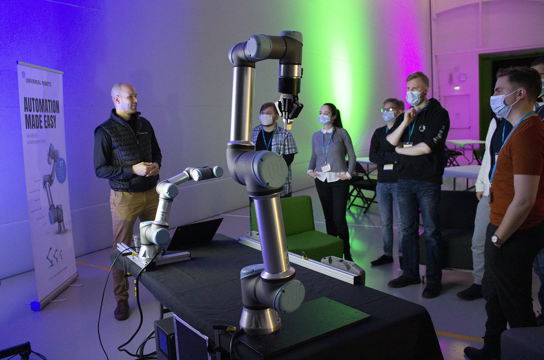 Yrityksen edustaja selostaa opiskelijoille haastetta robotin vieressä.