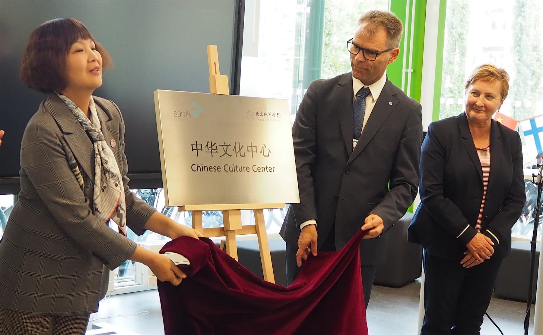 Ms. Wang Lin, Mr. Jari Multisilta and Ms. Aino-Maija Luukkonen revieling arts centre's sign.