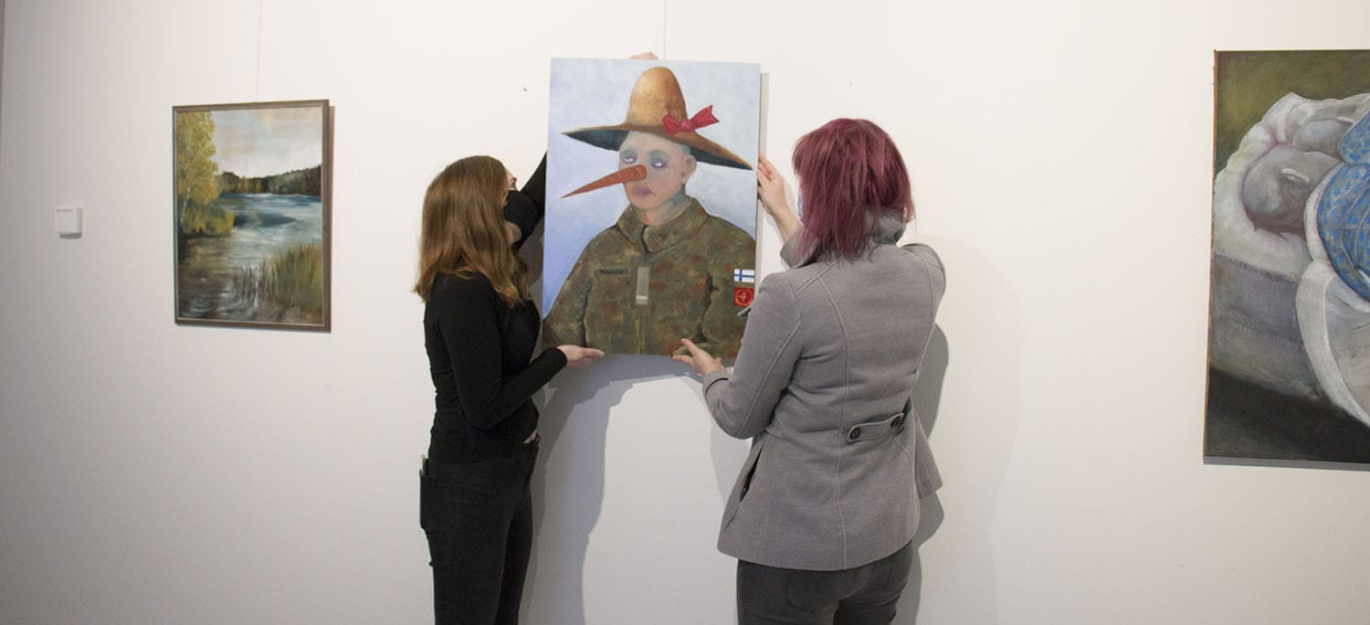 Kaksi naista ripustaa taideteosta SAMKin Porin kampuksen taidekäytävällä.
