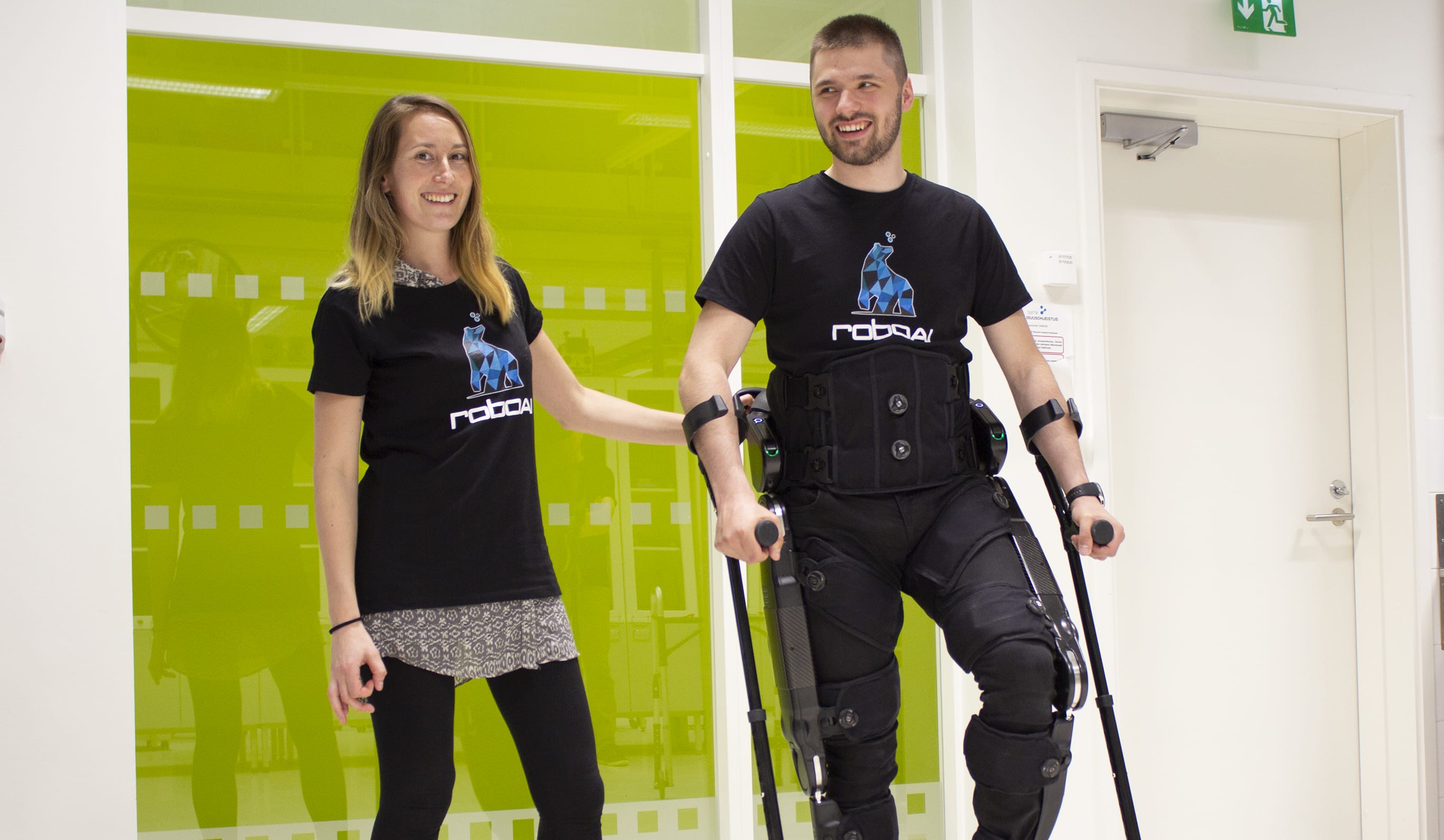A woman guides a man wearing an exoskeleton rehabilitation robot.