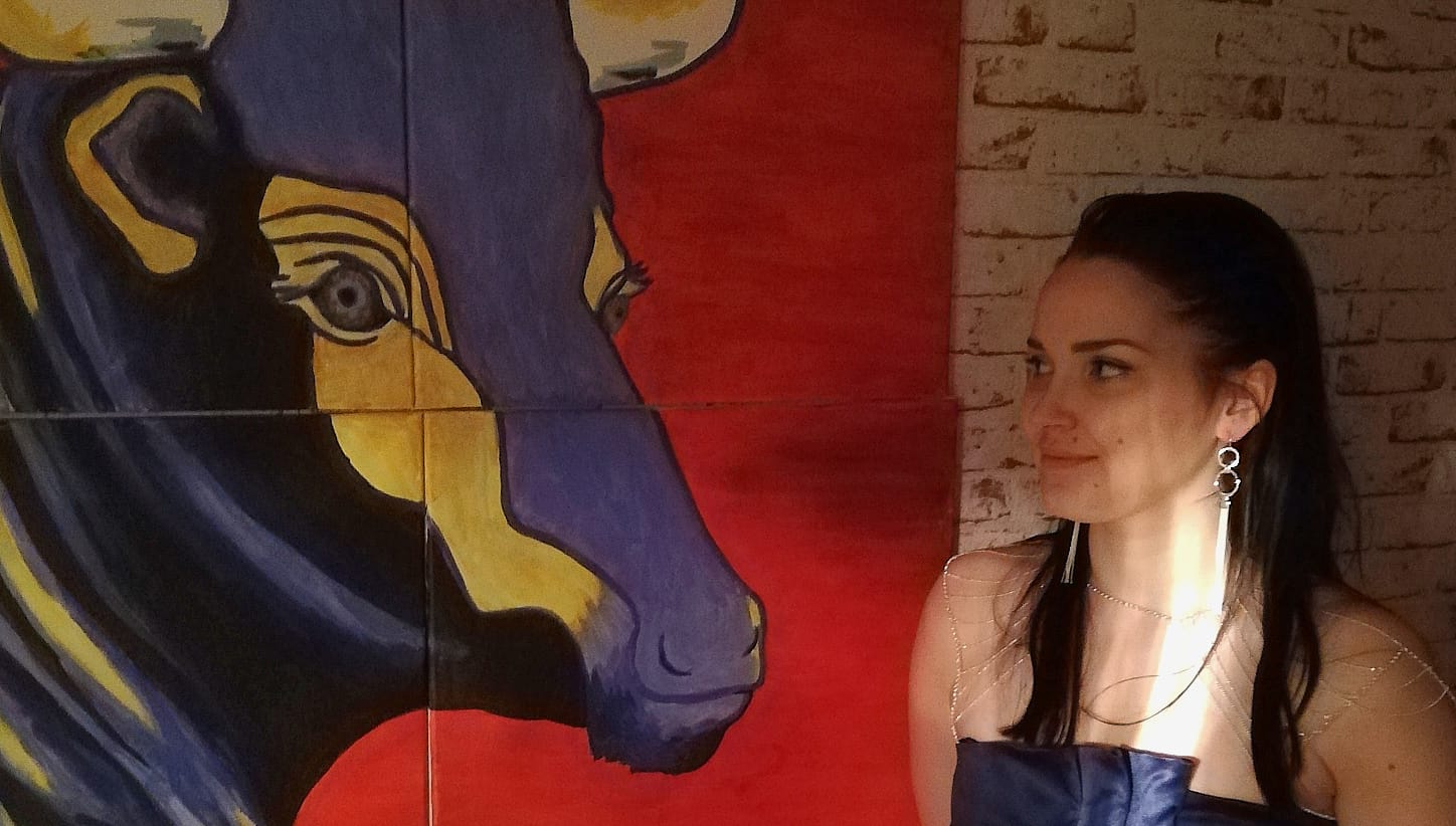 Janica Hakala lähikuvassa yhdessä lehmää kuvaavan maalauksen kanssa.