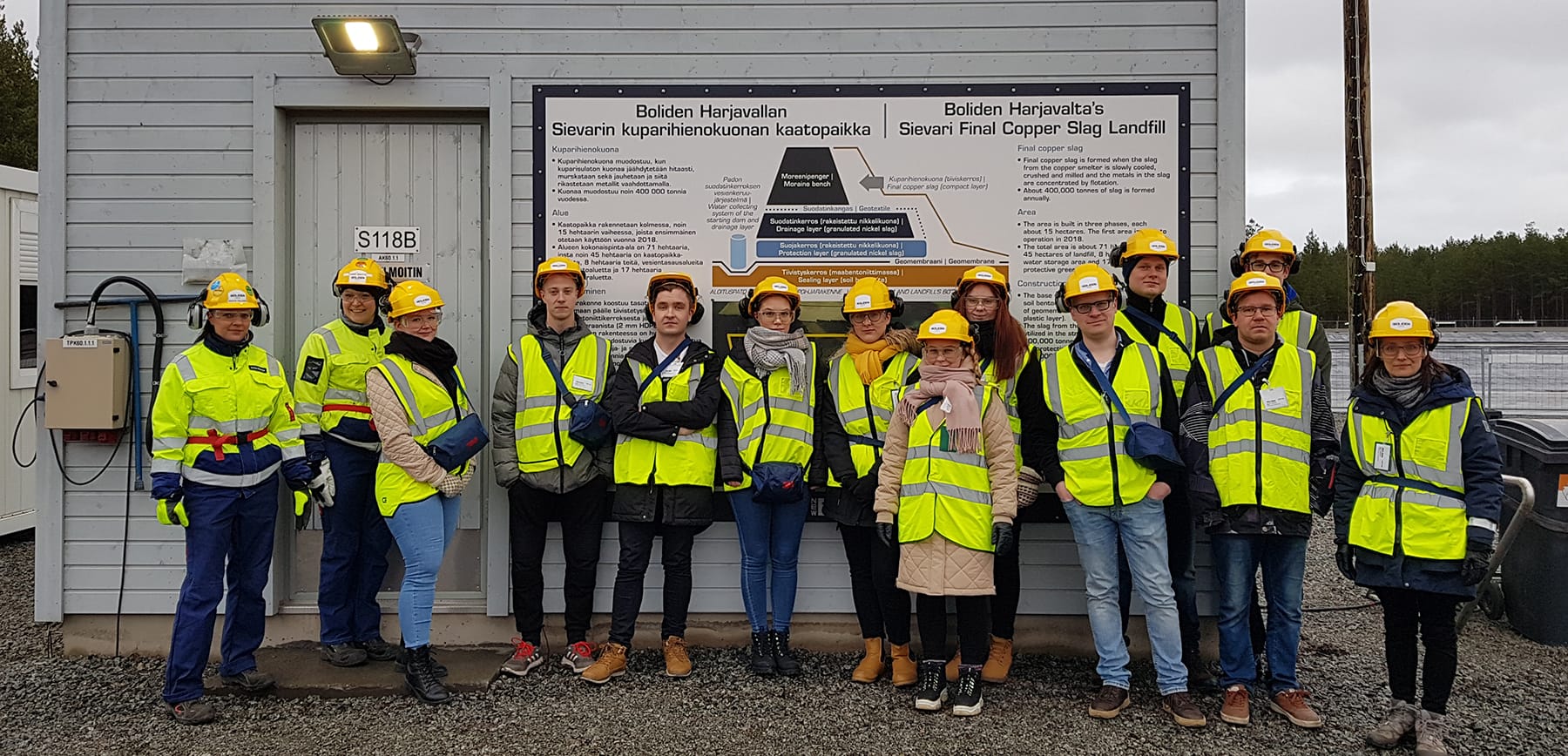 Student group wearing safety workwear and standing at copper slag landfill.