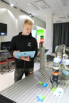 Opiskelija ohjaa robottia ohjaimella.