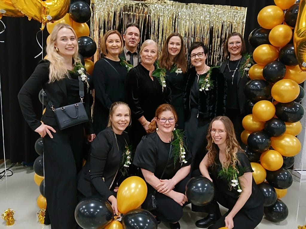 A group of people in front of a gold and black screen and balloons.