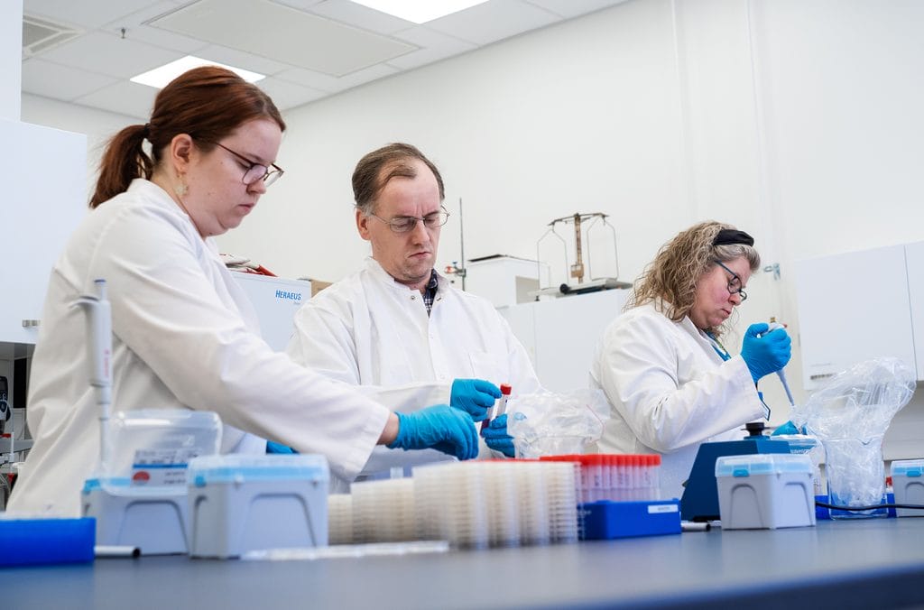 Kolme henkilöä työskentelee laboratoriossa valkoiset takit päällään.